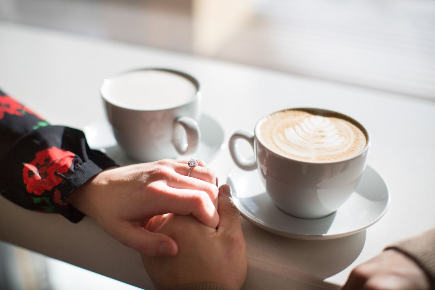 A person holds a white ceramic coffee cup with latte art on a light colored surface in natural lighting at Whitebark cafe in Banff, AB.