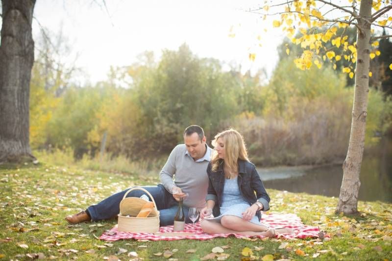 Couple enjoying a romantic autumn picnic on a red blanket by a pond, surrounded by colorful fall foliage at Fish Creek Park in Calgary.