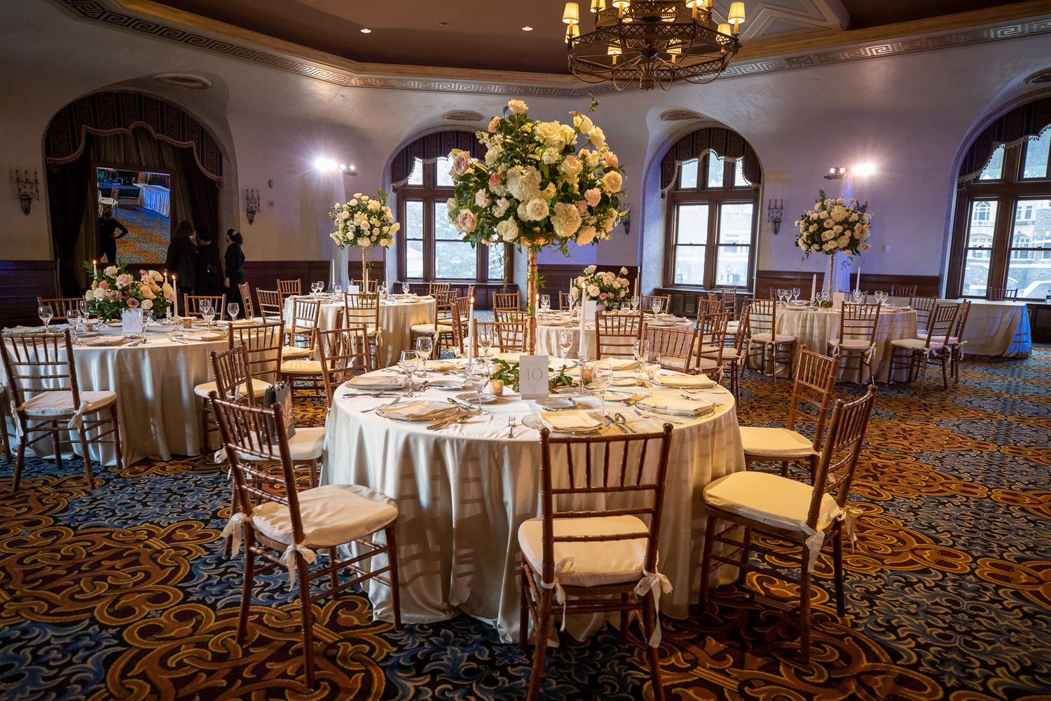 Elegant wedding reception ballroom with round tables, gold chiavari chairs and ornate chandeliers in warm lighting at Fairmont Banff Springs