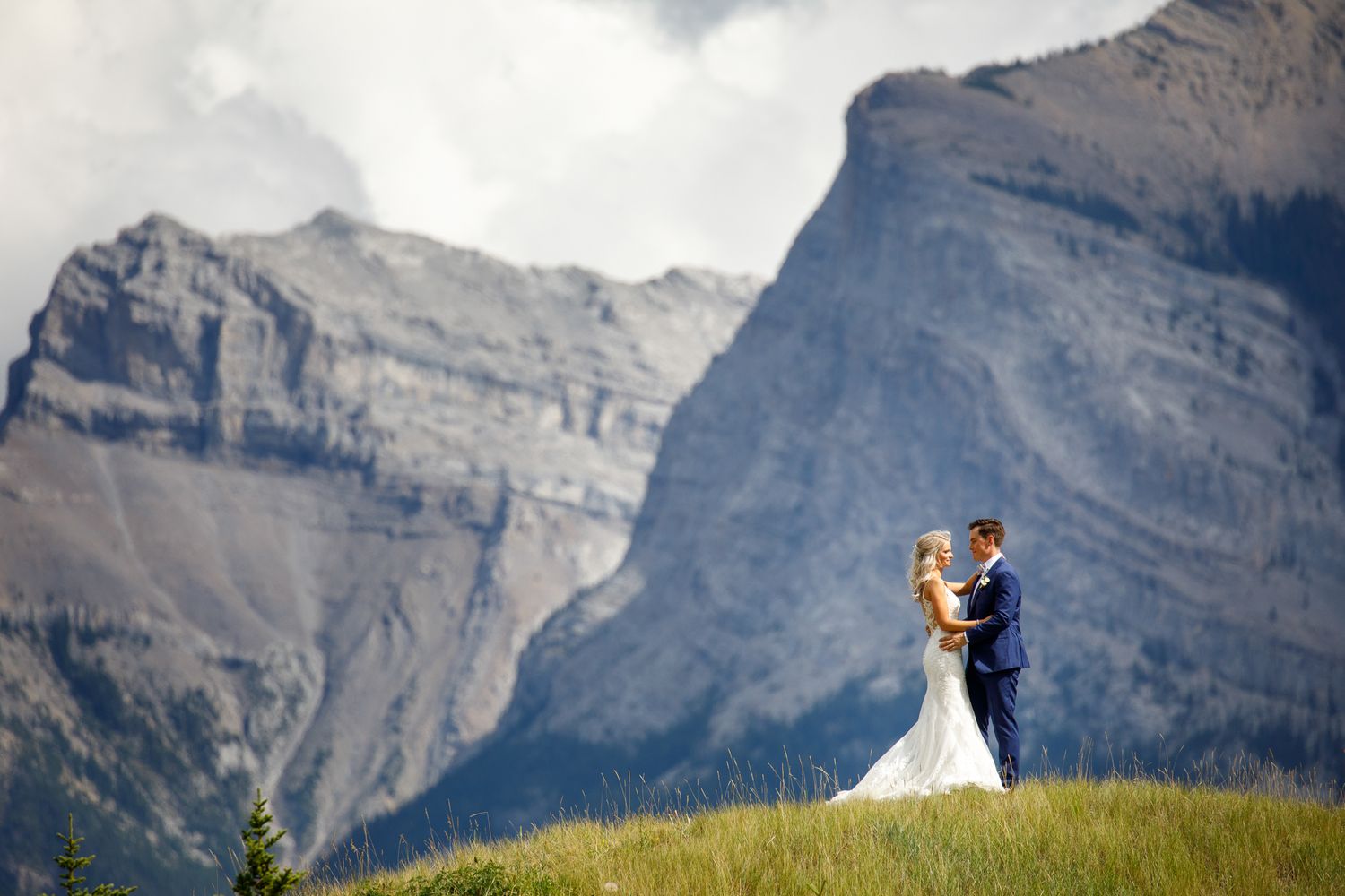 A wedding couple stands in front of majestic Rocky Mountain peaks at Tunnel Mountain in Banff National Park.