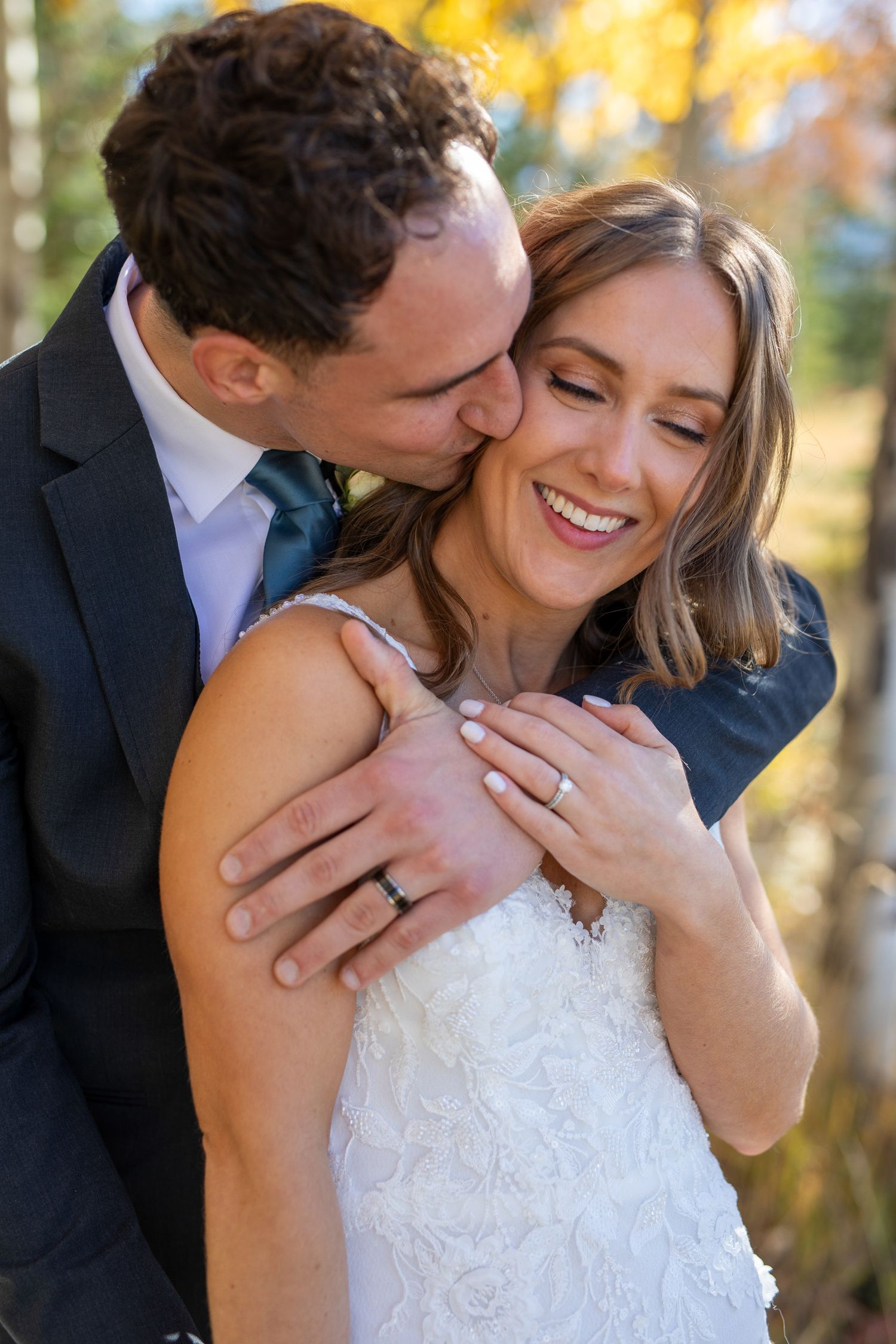 Romantic wedding couple embraces in autumn foliage with warm sunlight filtering through the trees at Benchland trail in Canmore, Alberta.