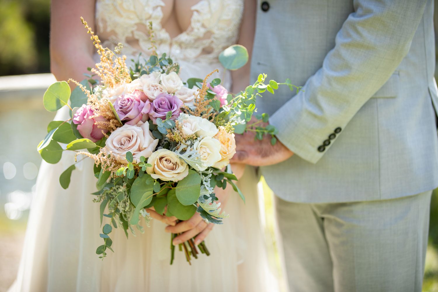 A wedding bouquets held against light colored formal wedding attire, featuring pink and purple flowers with greenery. Canmore ranch, Canmore