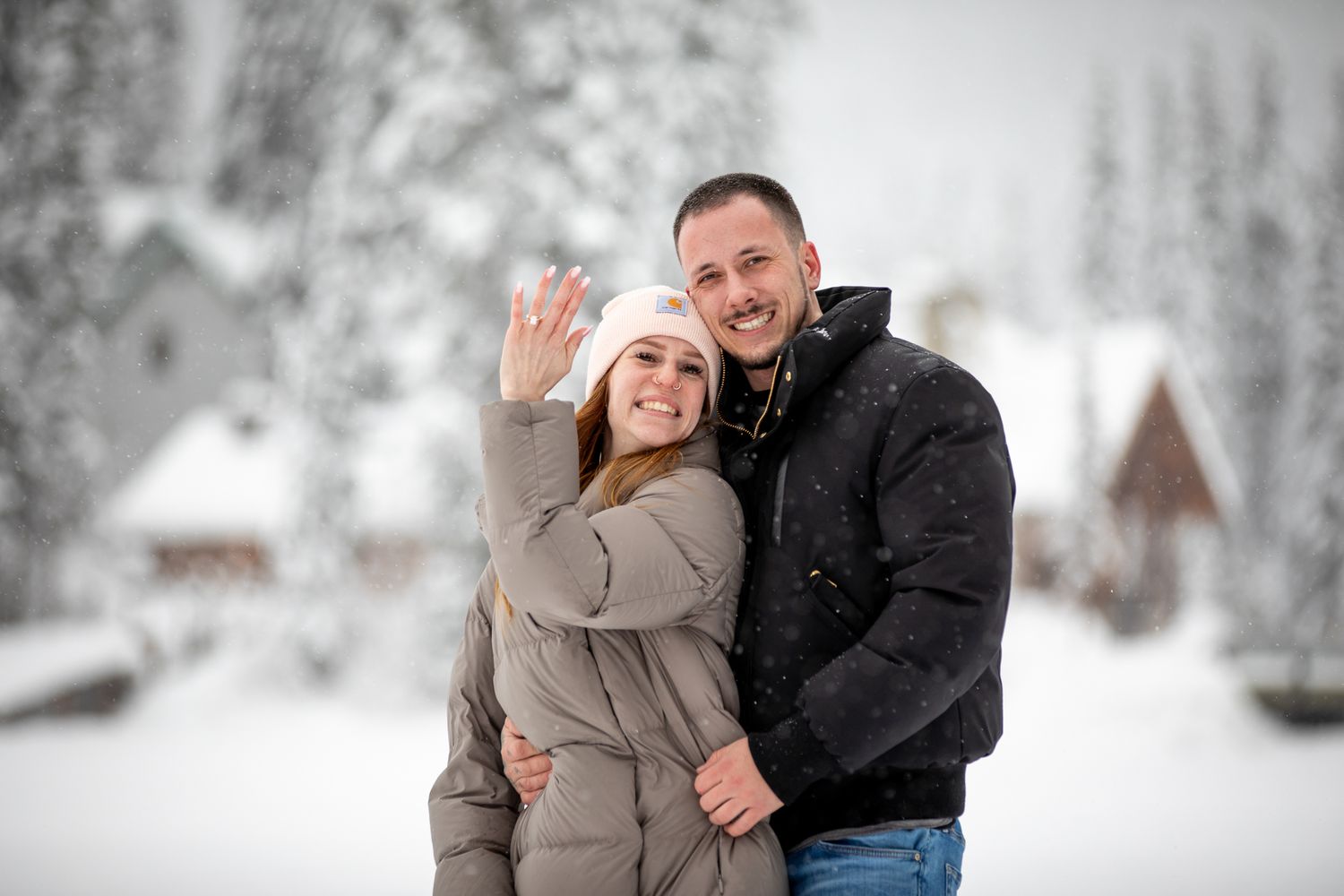A couple laughs and embraces during a winter photo session in the snow with trees in the background at Emerald Lake Lodge, in BC.