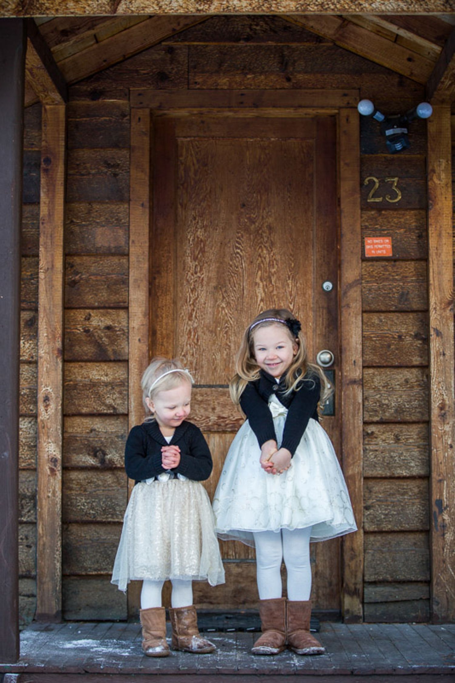 Two young children hanging on rustic wooden cabin wall with vintage style lighting and decor in Banff, AB.