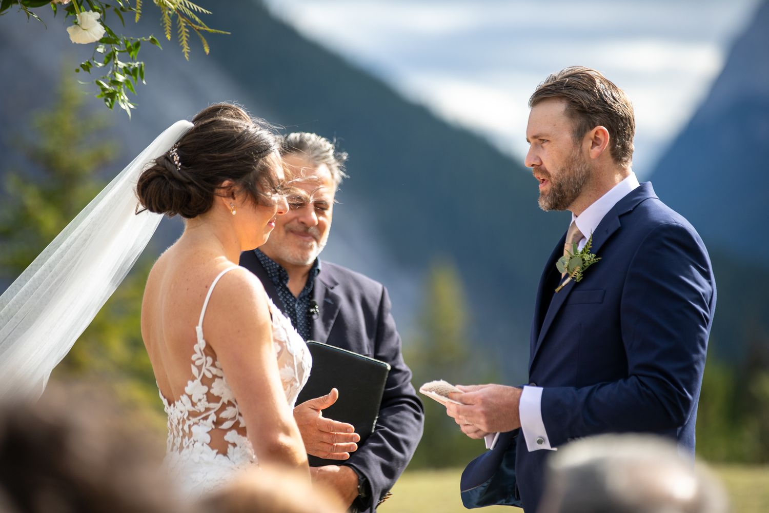 A couple exchanges vows during an outdoor mountain wedding ceremony with scenic natural backdrop. Tunnel Mountain Reservoir Banff, AB