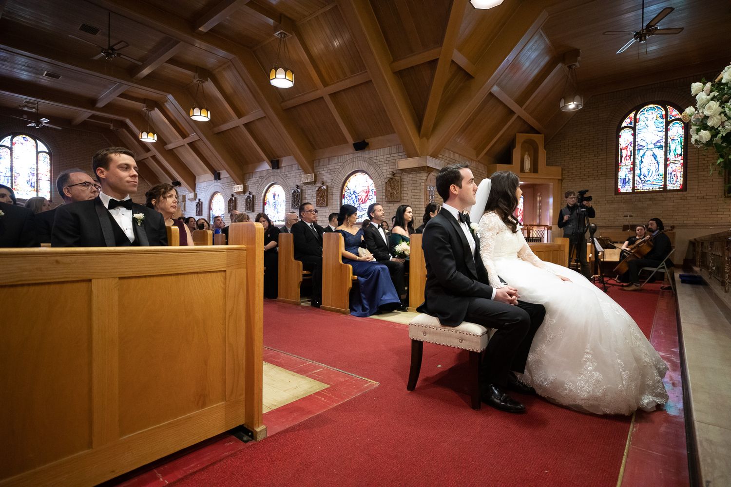 Wedding ceremony taking place in a traditional church sanctuary with wooden beams and stained glass windows.