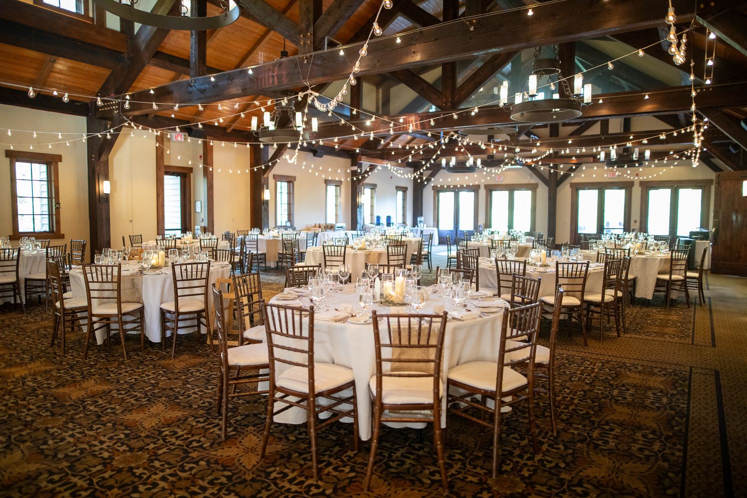 Elegant wedding reception venue with round tables, gold chiavari chairs and twinkle lights hanging from wooden beams at Silvertip resort.