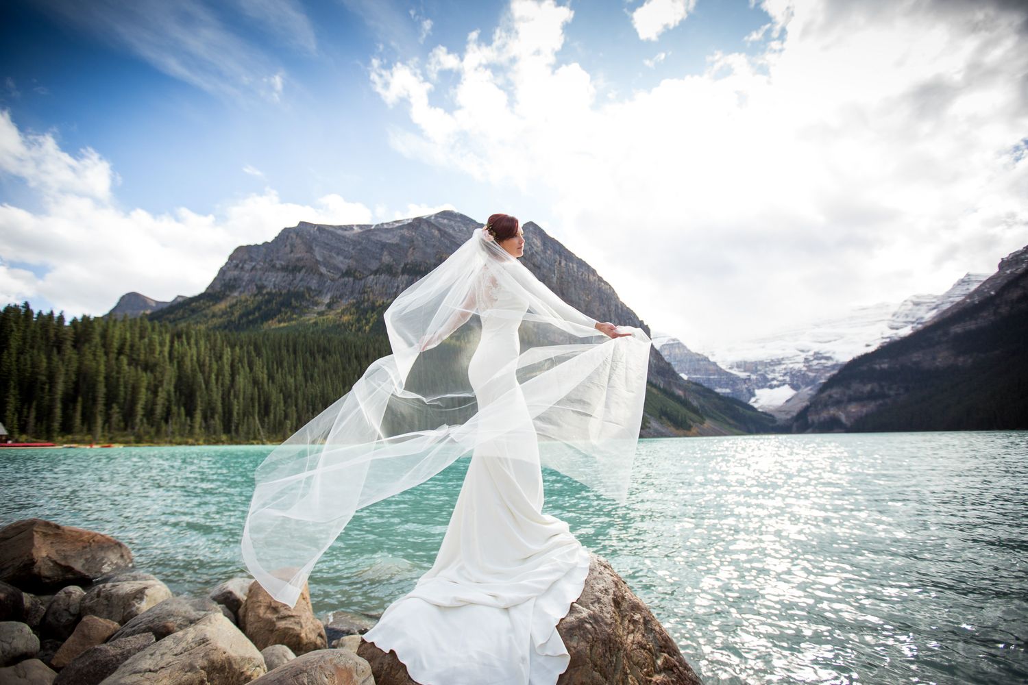 A flowing white dress billows in the wind against the backdrop of Lake Louise and majestic Rocky Mountains in Banff.