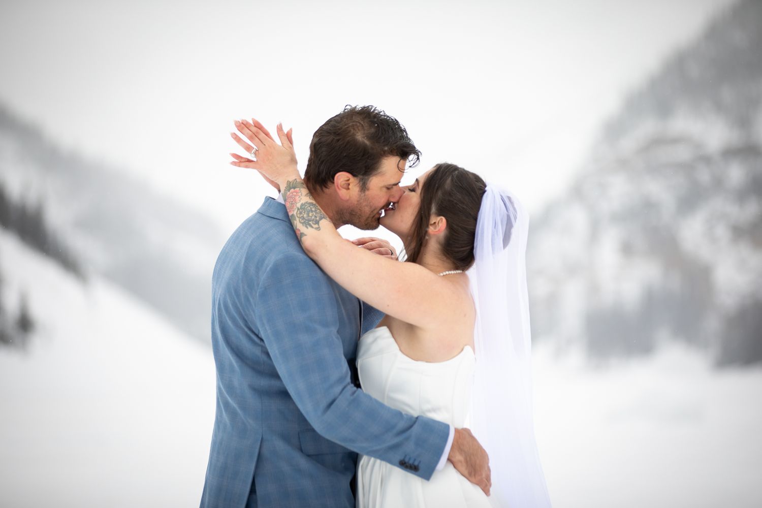 A romantic winter wedding scene with a couple embracing in front of a snowy mountain landscape at Lake Louise, Alberta.