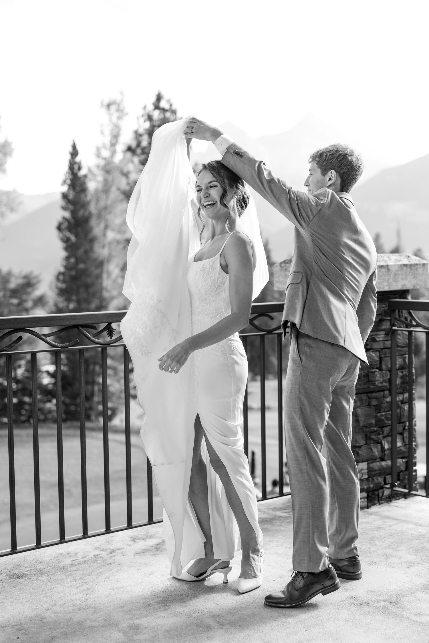 A black and white wedding photo of a couple dancing on a balcony with mountain views in the background at Silvertip resort in Canmore, AB.