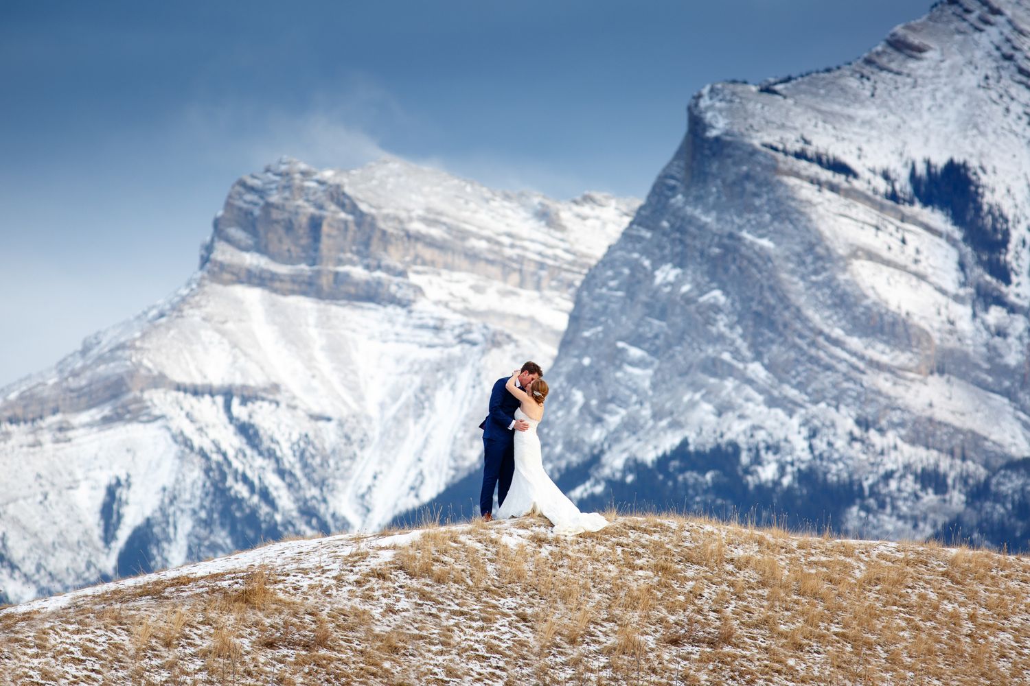 A wedding couple poses together in snowy Three Sisters mountain landscapes during their winter wedding photo session in Canmore, Alberta.