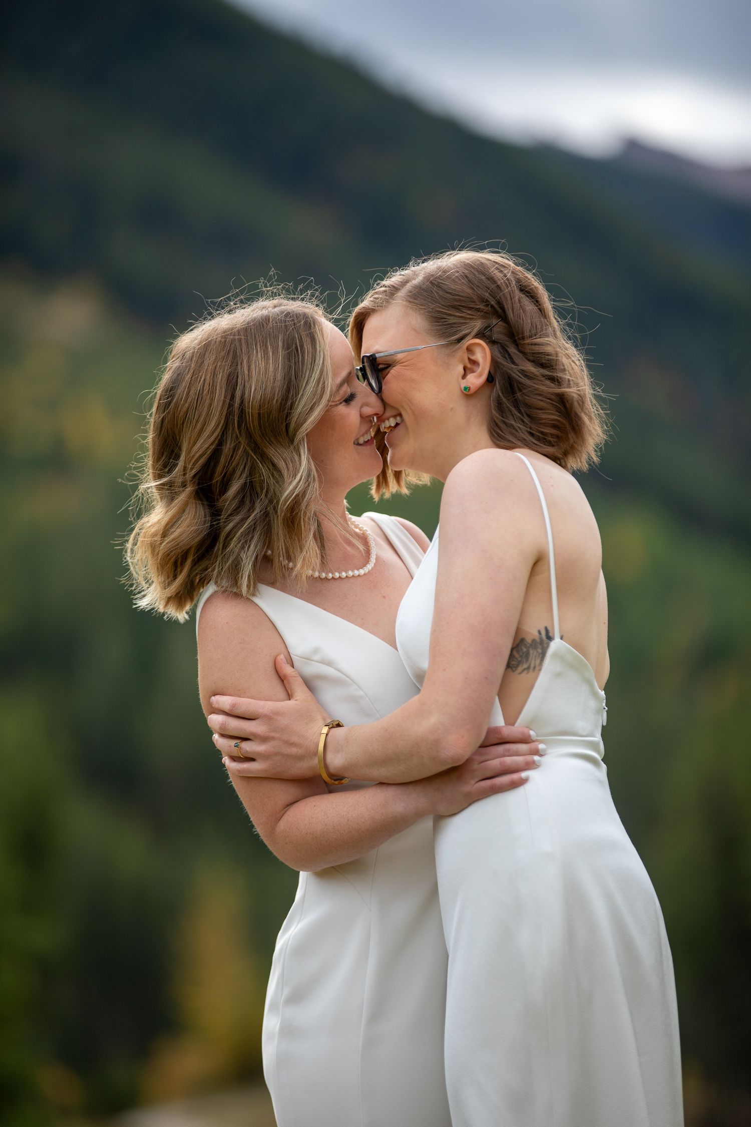 Two brides in white dresses share an intimate moment against a mountainous backdrop at Earl Grey Lodge in Panorama, BC