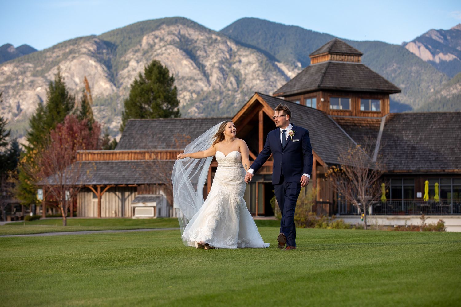 A couple in wedding attire walks together at Eagle Ranch resort with mountains background. Invermere, British Columbia.