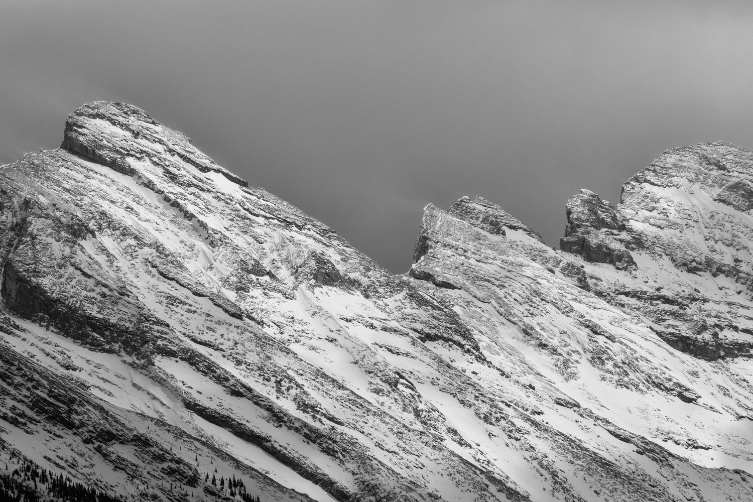 Black and white photo of rugged snow-dusted mount Rundle peak against a dramatic grey sky in Banff National Park.