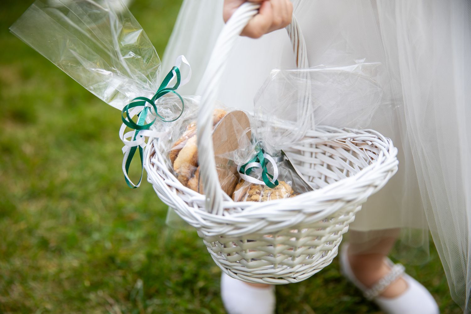 A white woven basket filled with wedding favors wrapped in clear cellophane and tied with turquoise ribbons.