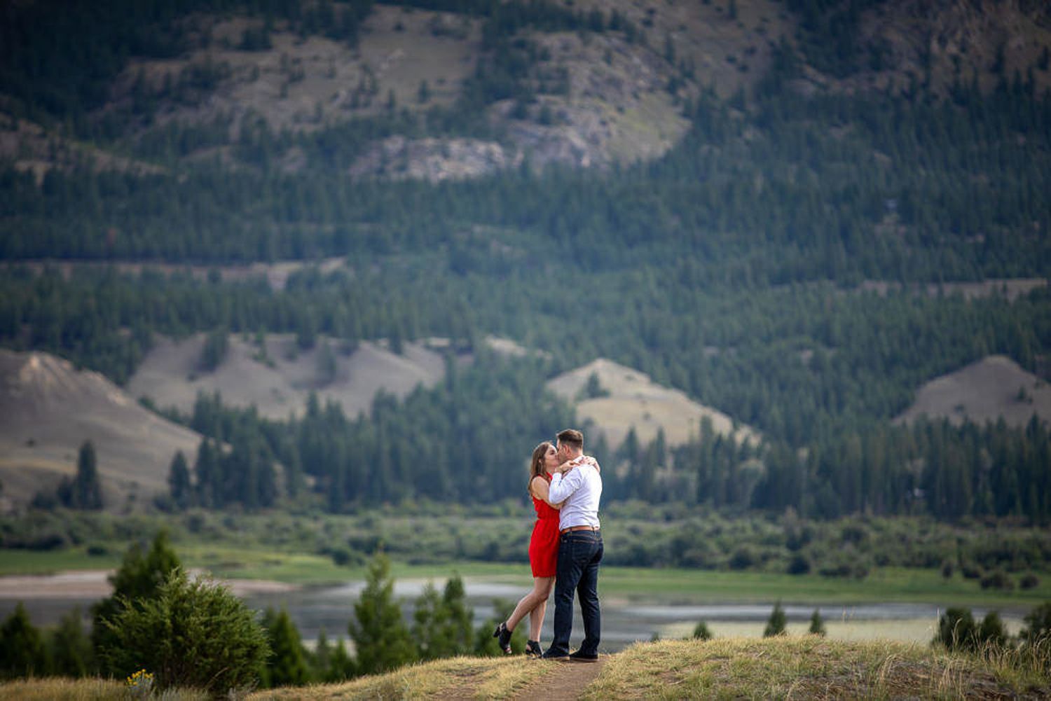 A couple embraces during their engagement photo session in a scenic mountain valley landscape at sunset in Wetland Reserve in Invermere, BC.