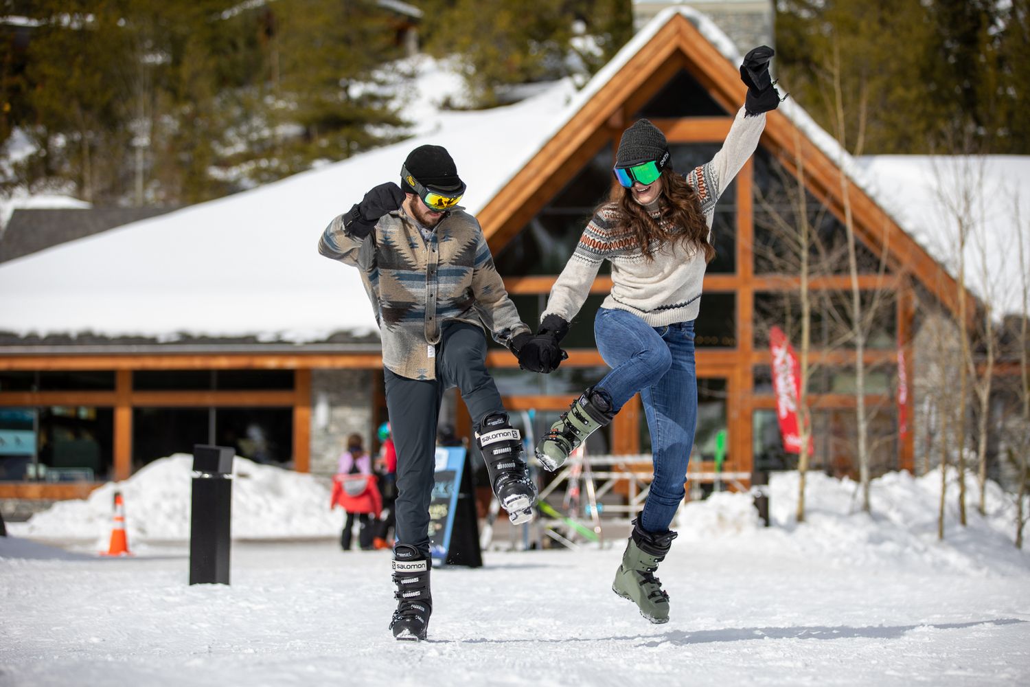 A skateboarder performs tricks on a snowy terrain with wooden buildings in the background at Grey Wolf Panorama, BC