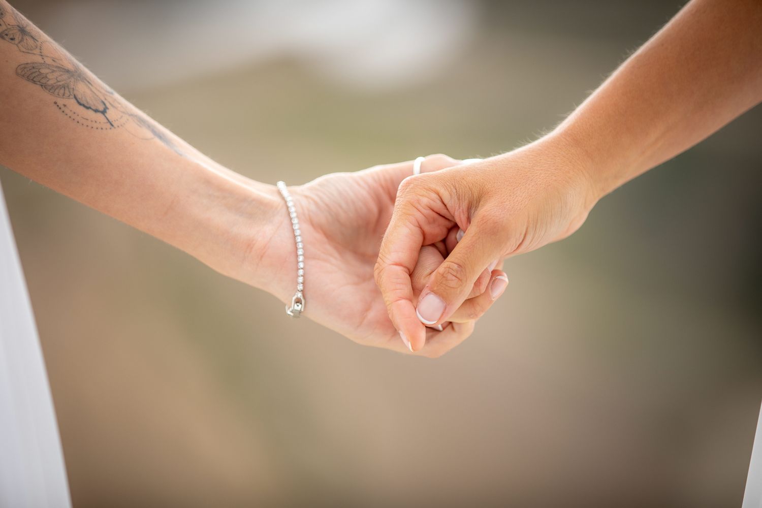 Close-up of hands exchanging wedding rings during an outdoor ceremony with sunlight in the background.