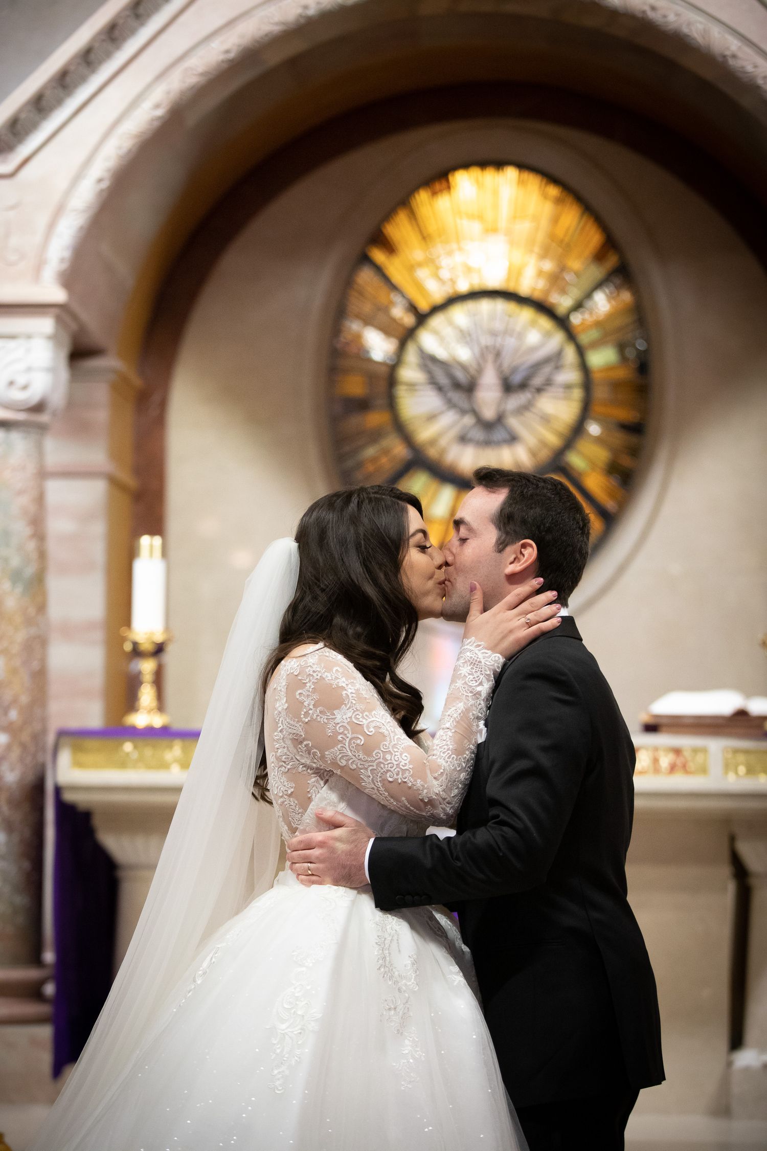 A romantic wedding kiss sequence captured in a church with a stained glass window and dove motif in the background St Mary's Church in Banff