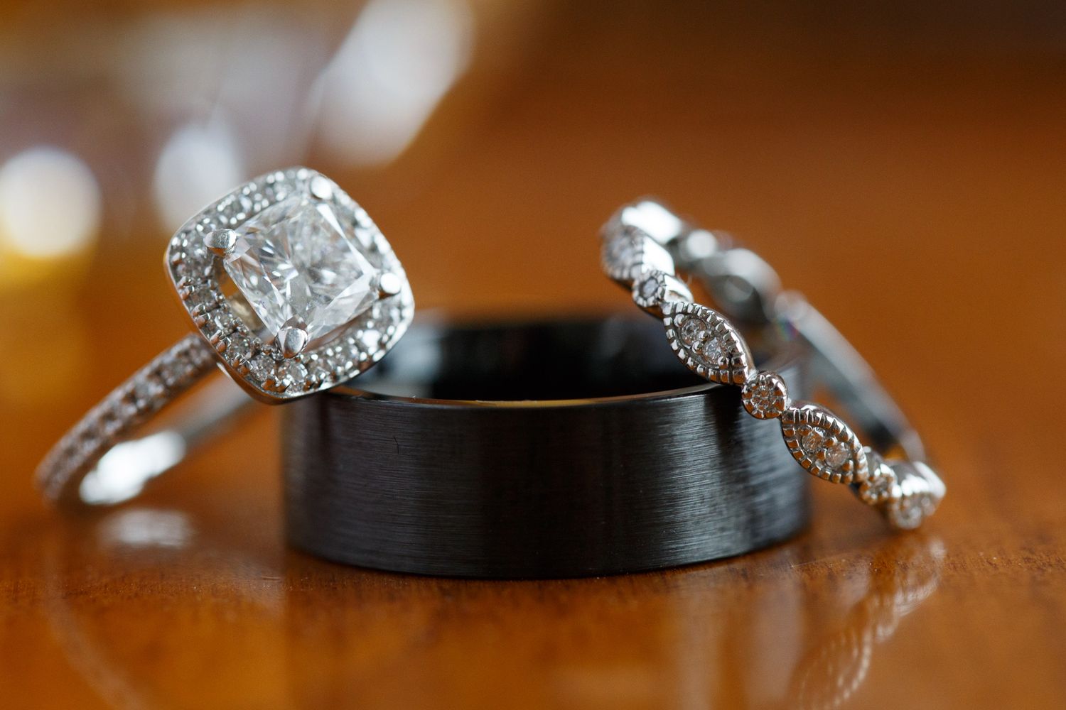 Three wedding rings displayed together, featuring a diamond halo engagement ring, black tungsten band, and diamond accent ring.