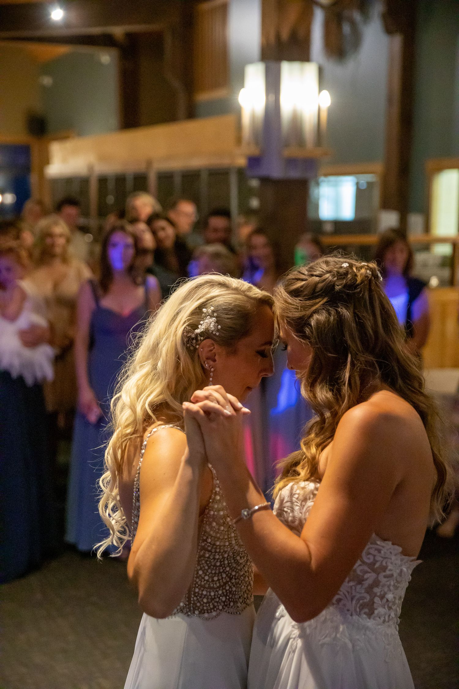 Two brides share their first dance at a wedding reception, surrounded by guests in a warmly lit Eagle Eye venue at Kicking Horse Resort, BC