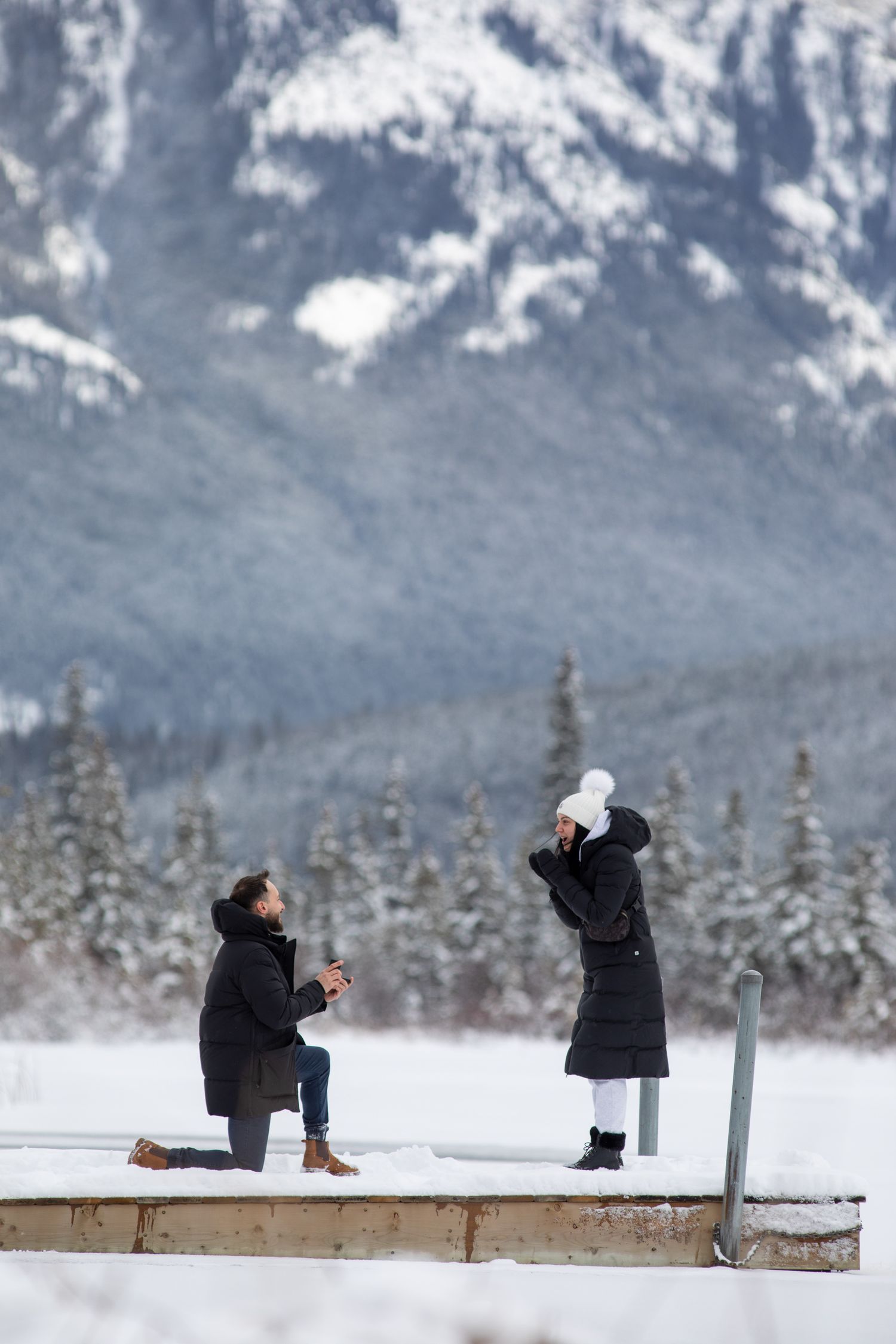 A sequence of winter proposal photos showing a couple on a snowy dock with mountains in the background.   Vermilion lakes in Banff. AB