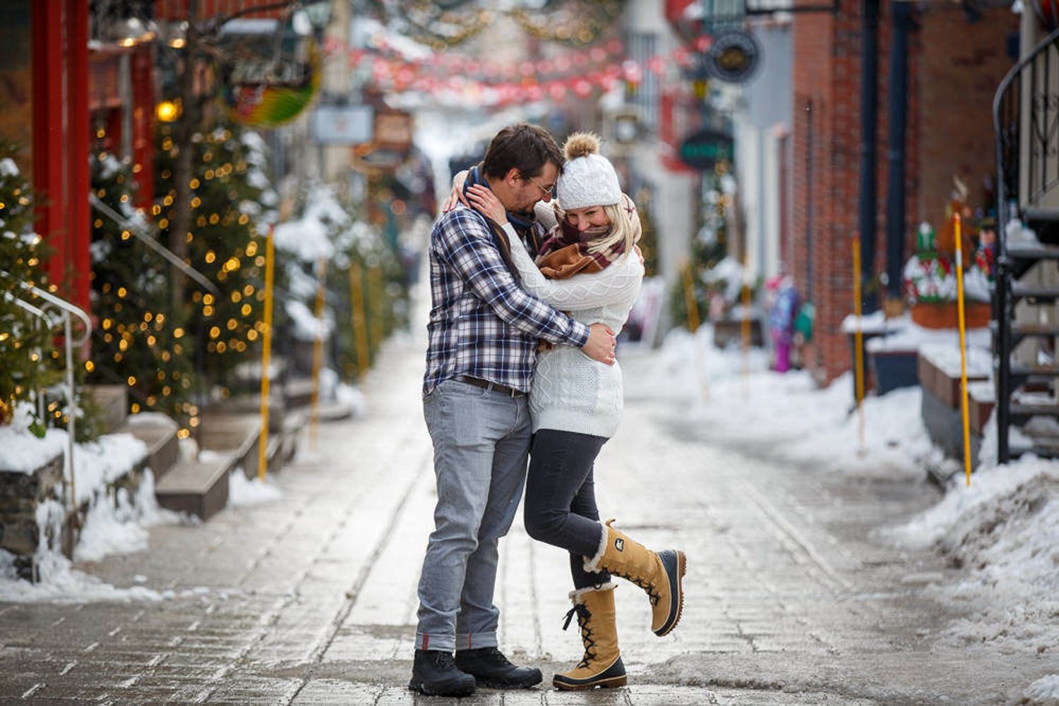 A couple embraces on a snowy winter street decorated with holiday lights and decorations in a charming town of Old Quebec City.