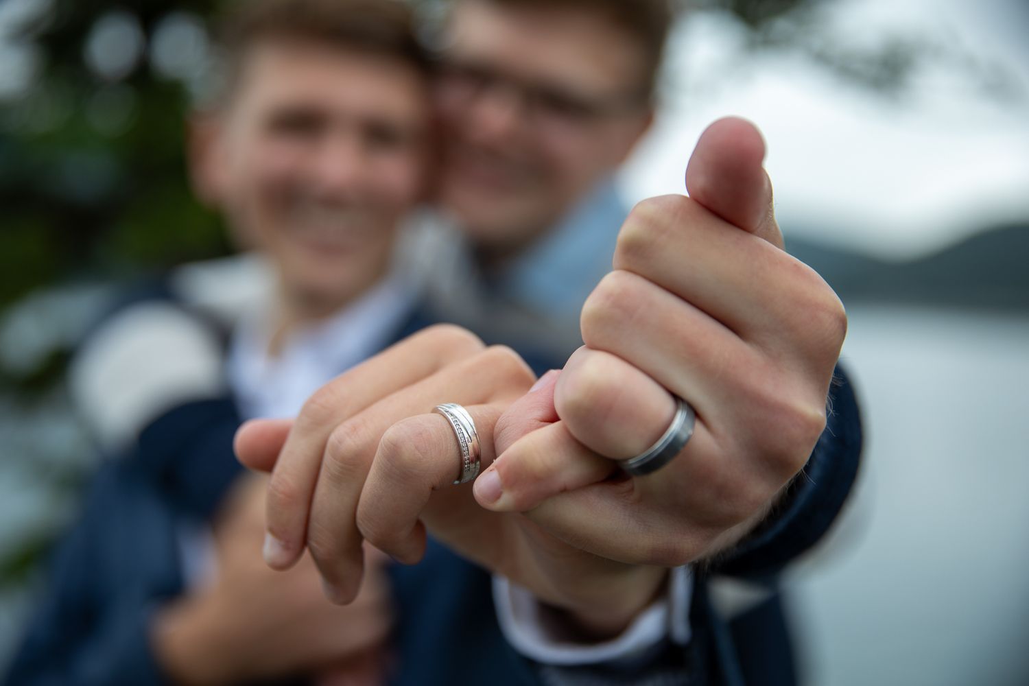 A close-up shot of hands holding a small ring against a blurred outdoor background. Banff
