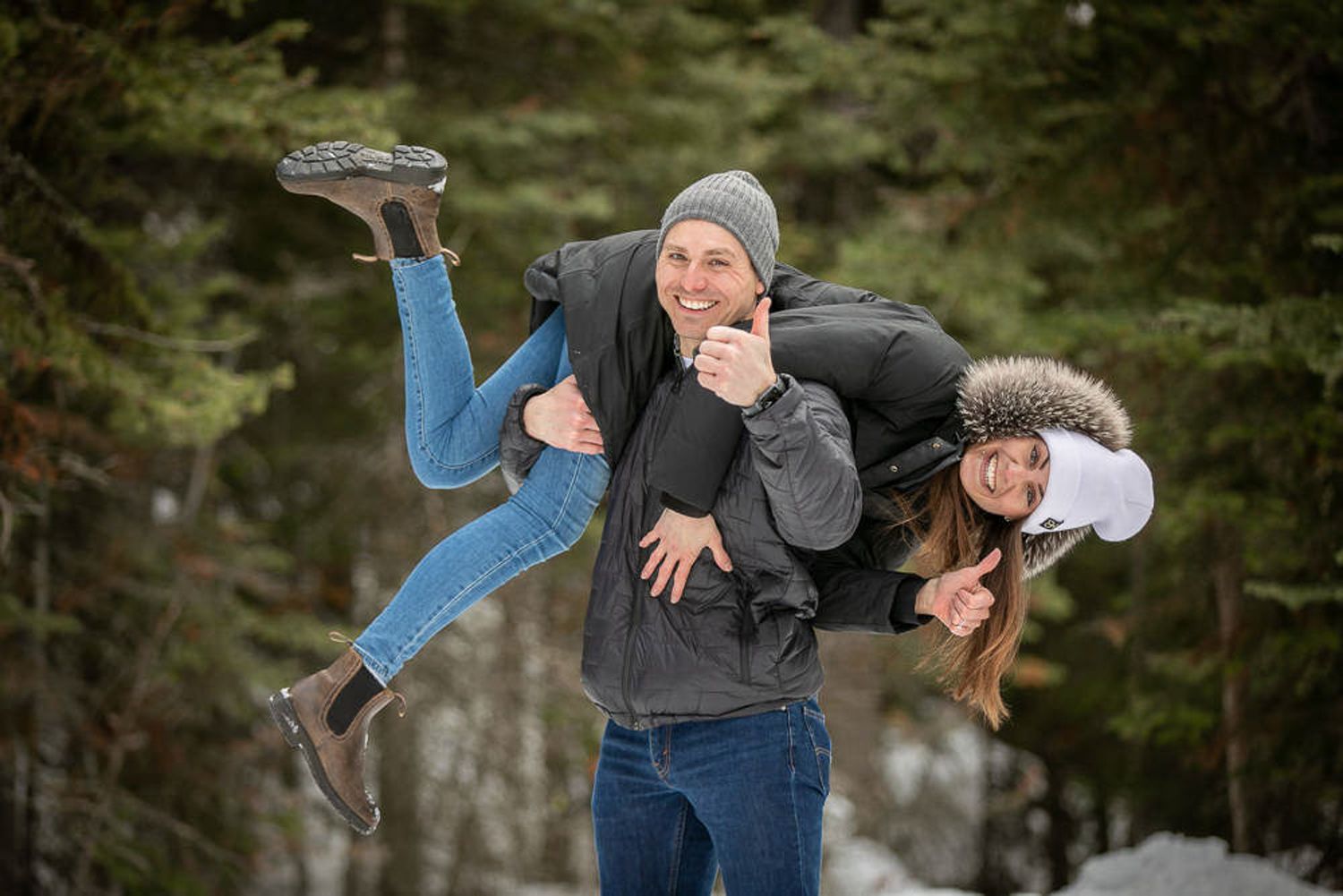 Two newly engaged couple together outdoors in a playful and energetic pose against a green forest backdrop in Lake Louise, AB.