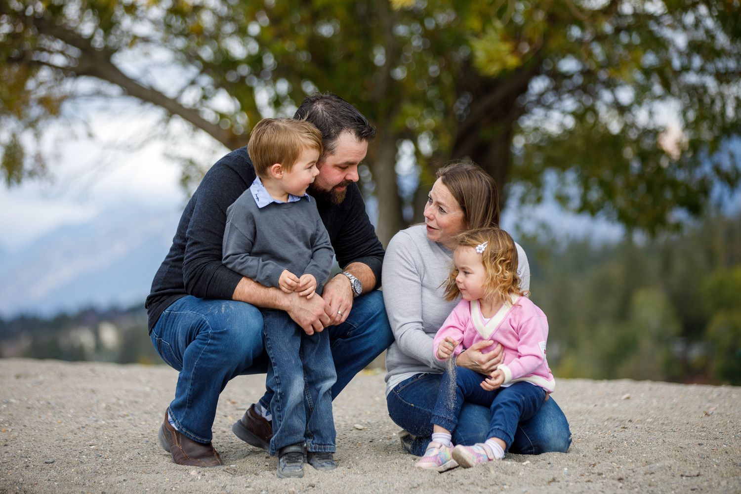 Family in casual attire sits together on a stone path during an outdoor photo session Timber Ridge in Windermere, BC