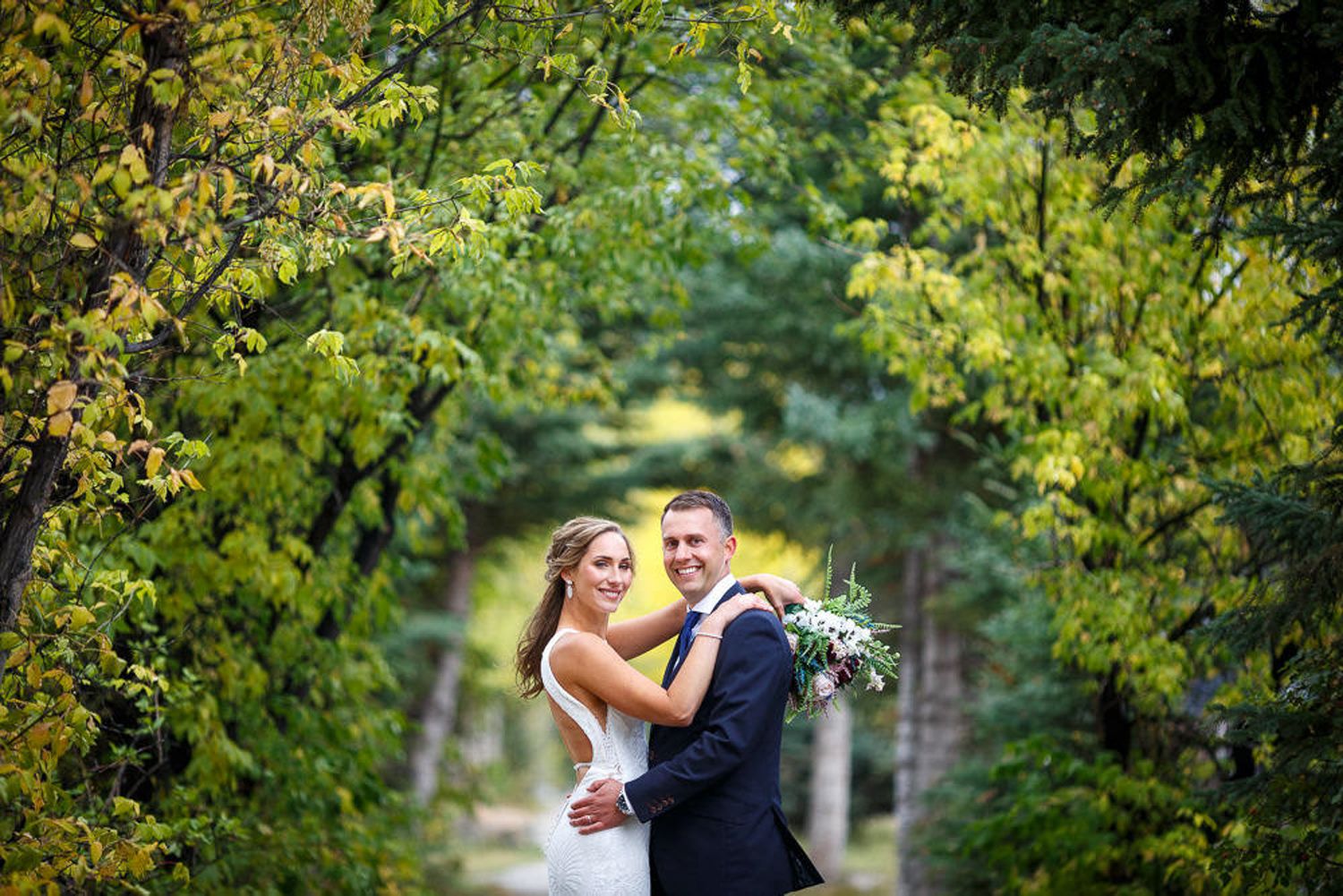 A couple shares a romantic moment surrounded by lush green foliage in a garden setting. Old engine bridge in Canmore, Alberta.