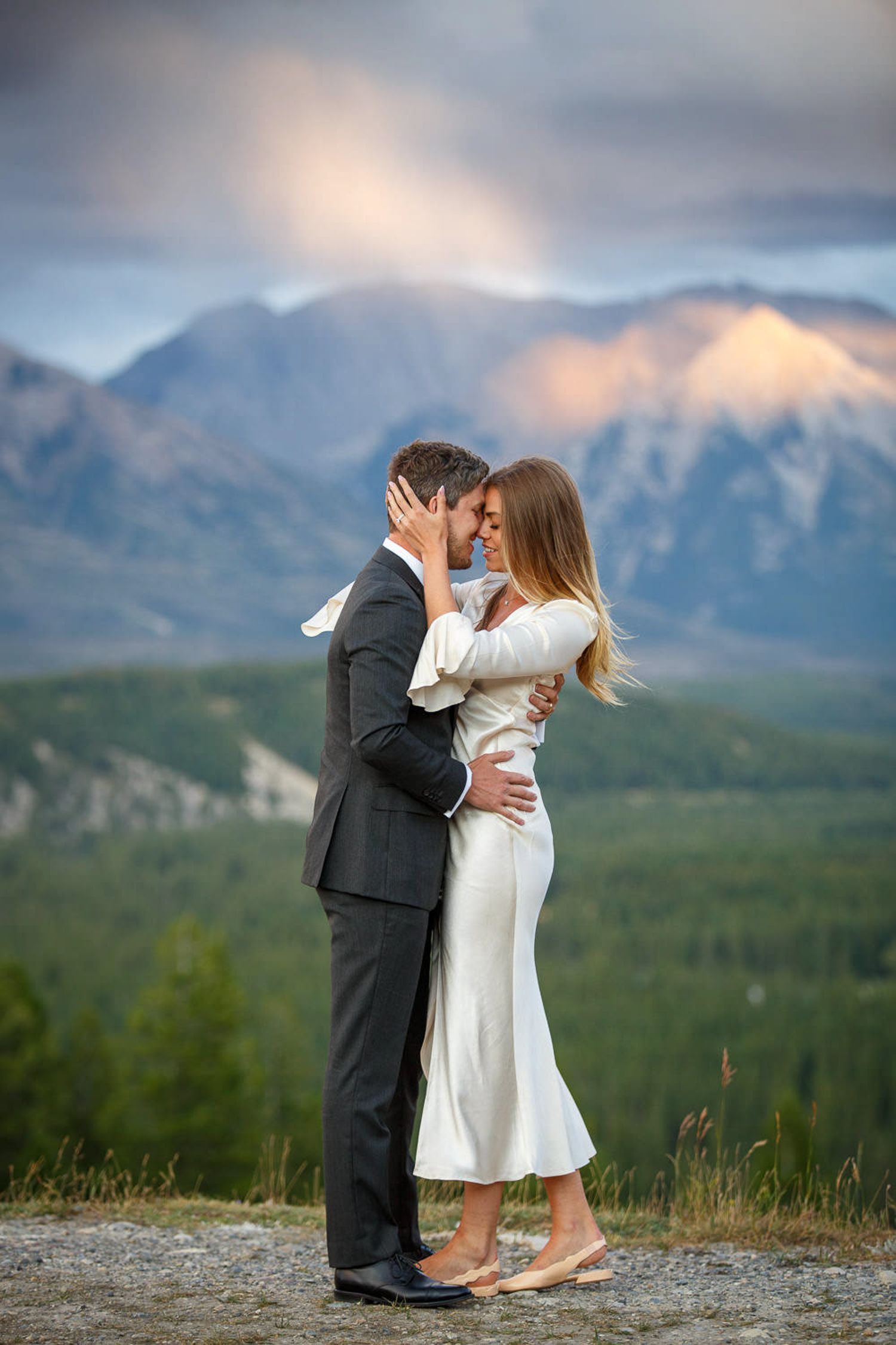 A couple shares a romantic kiss against a stunning mountain landscape backdrop in Banff National Park.