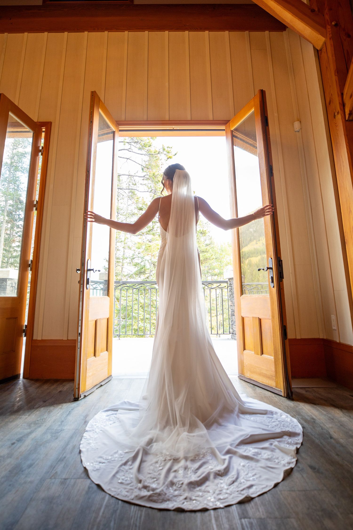 A stunning wedding dress with a long flowing train is showcased in a series of silhouette shots against wooden doors and floors at Silvertip