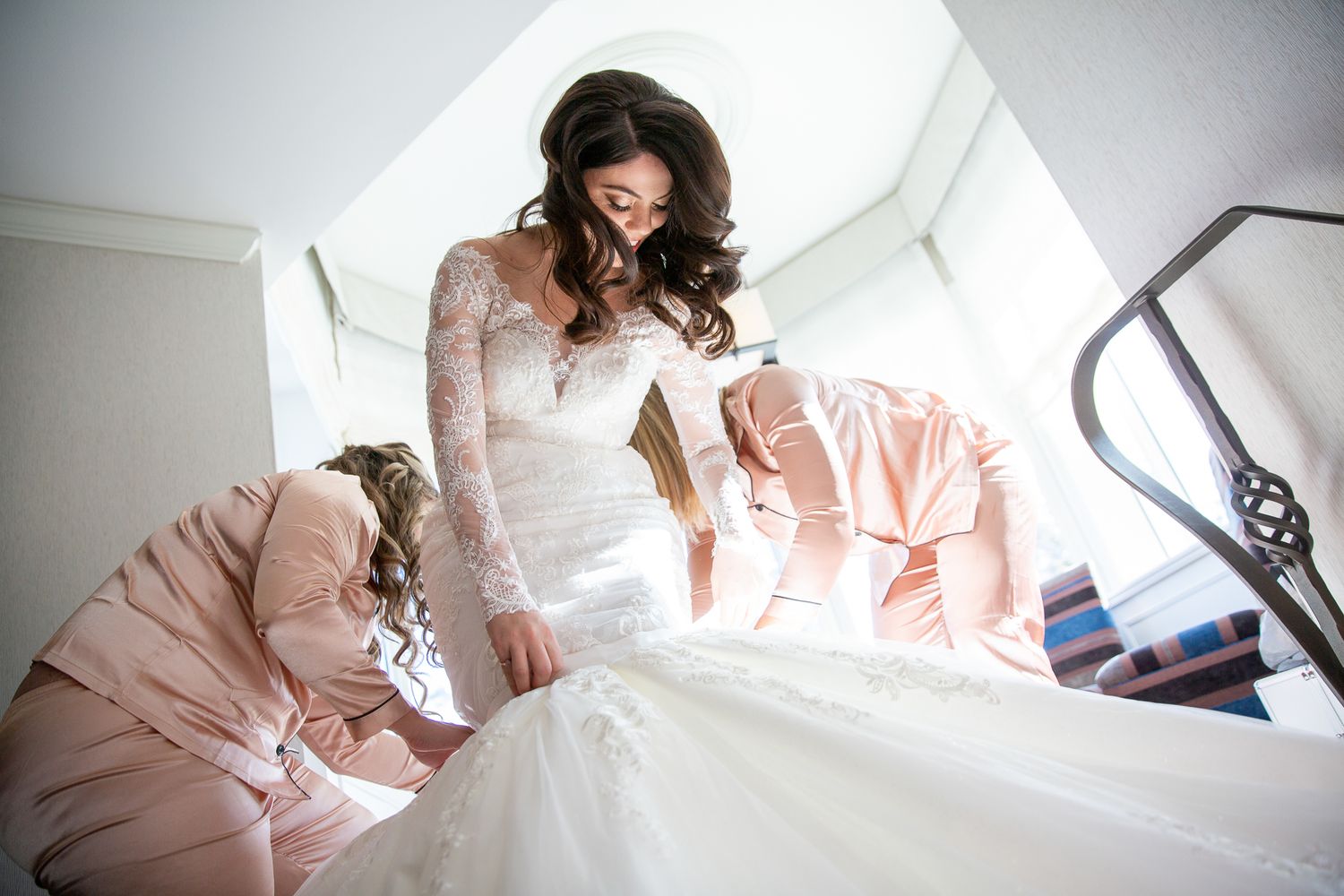 Bride in a flowing white wedding dress sits elegantly on a light-colored couch in a bright room. Fairmont Banff Springs Hotel.