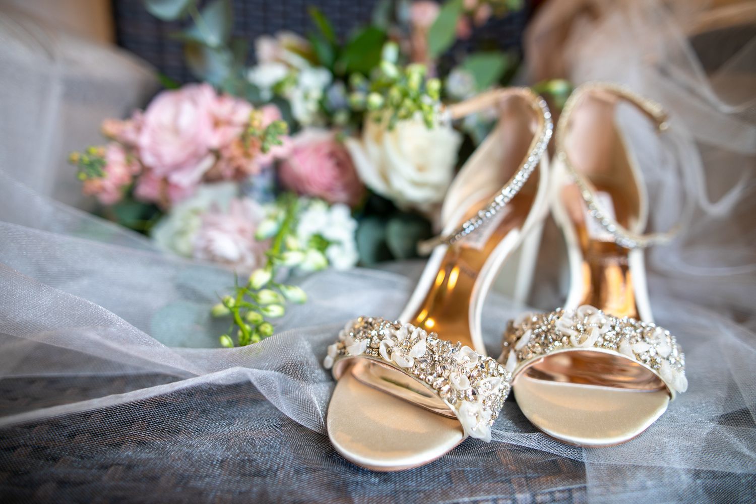 A collection of elegant bridal accessories including beige sandals, flowers, and delicate lace details arranged on a surface. Canmore, AB.