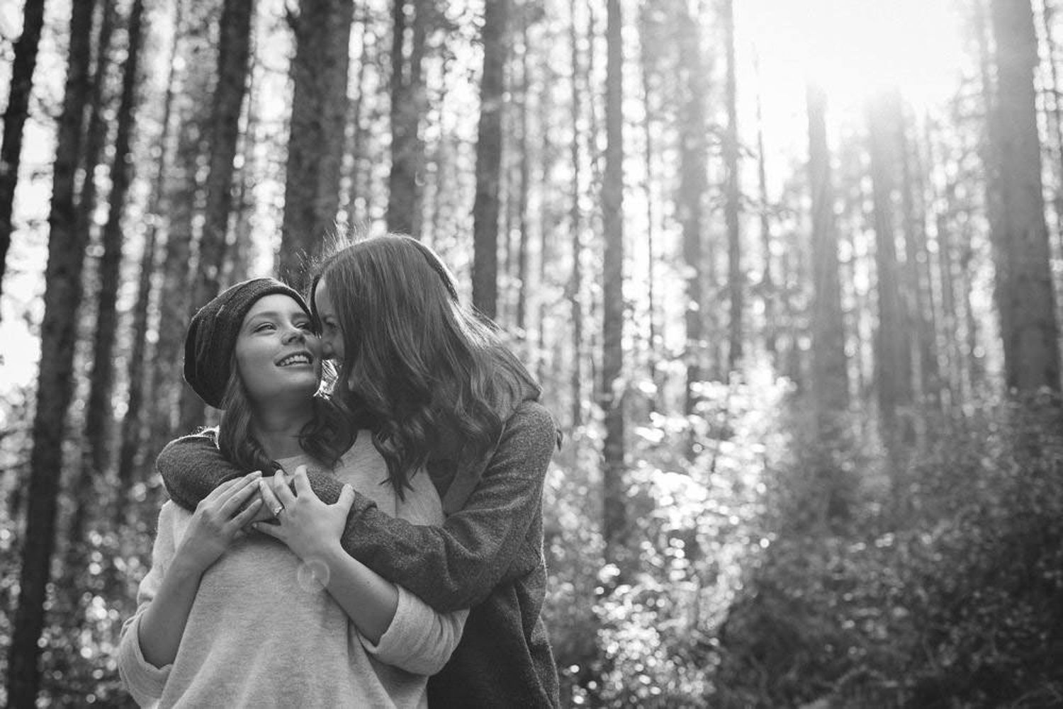 A couple shares a joyful moment while walking through a sunlit forest with tall trees  in Kananaskis Country in Alberta.