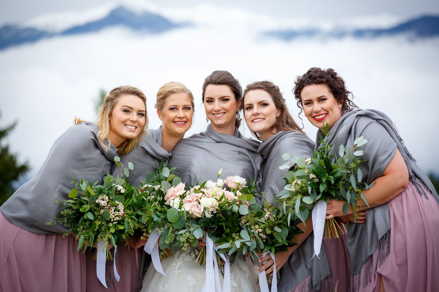 Bride and four bridesmaids in gray shawls holding bouquets with misty mountain backdrop at Cherry creek estate