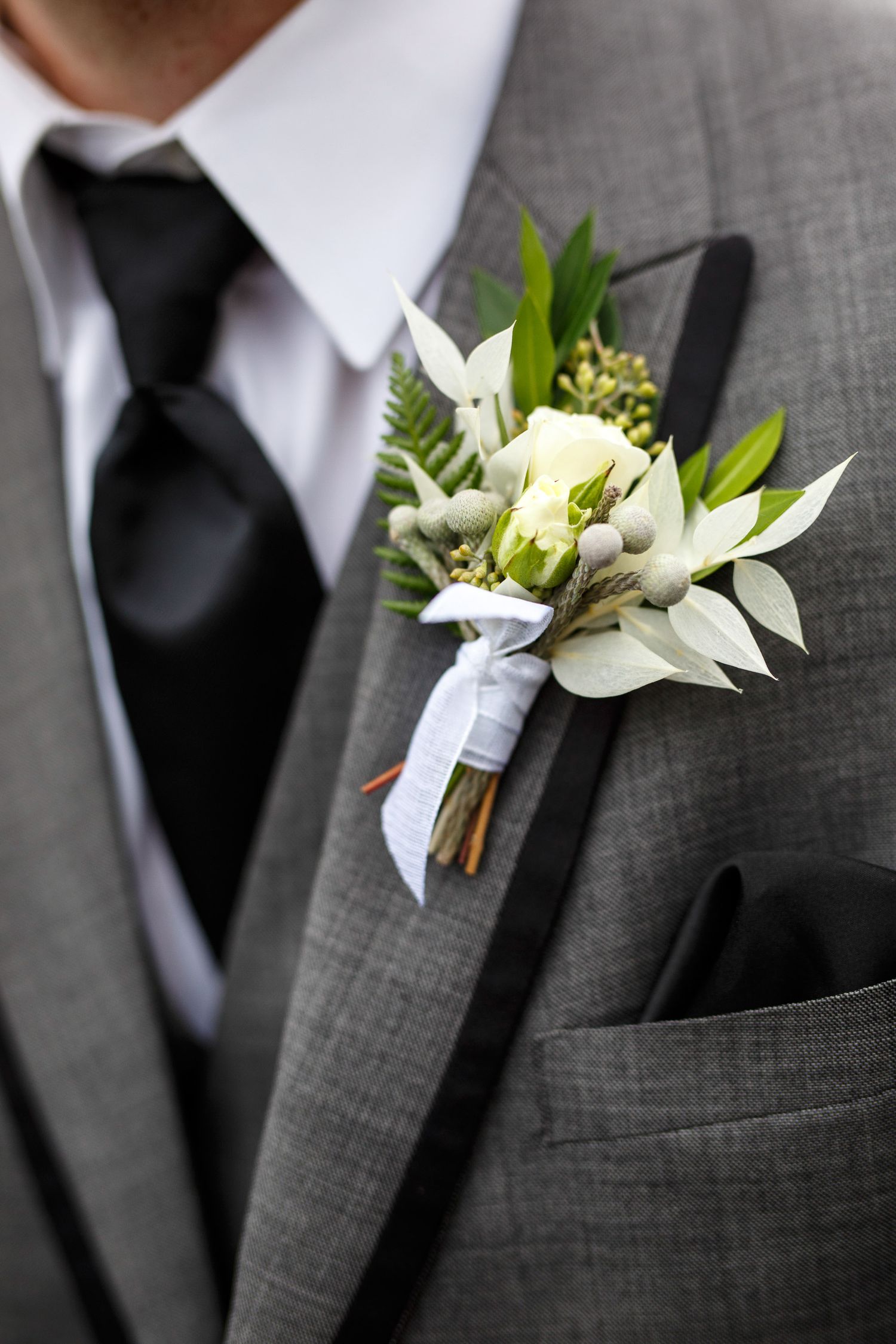 Groom in gray suit with white rose boutonniere, black tie, and pocket square at a wedding. Cherry creek estate