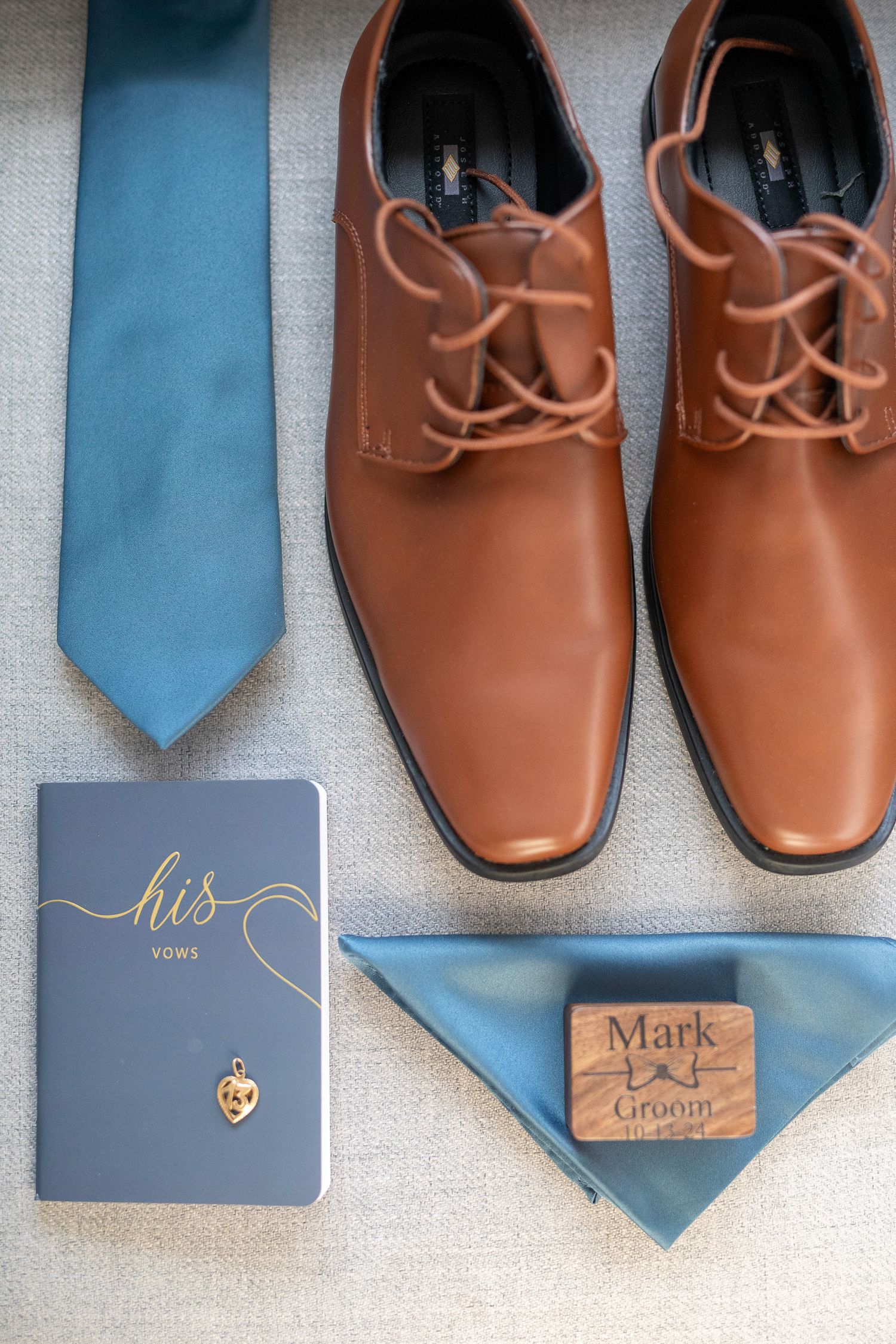 Wedding accessories including brown leather dress shoes, blue neckties, and personalized groom details laid out on grey surface. Canmore.