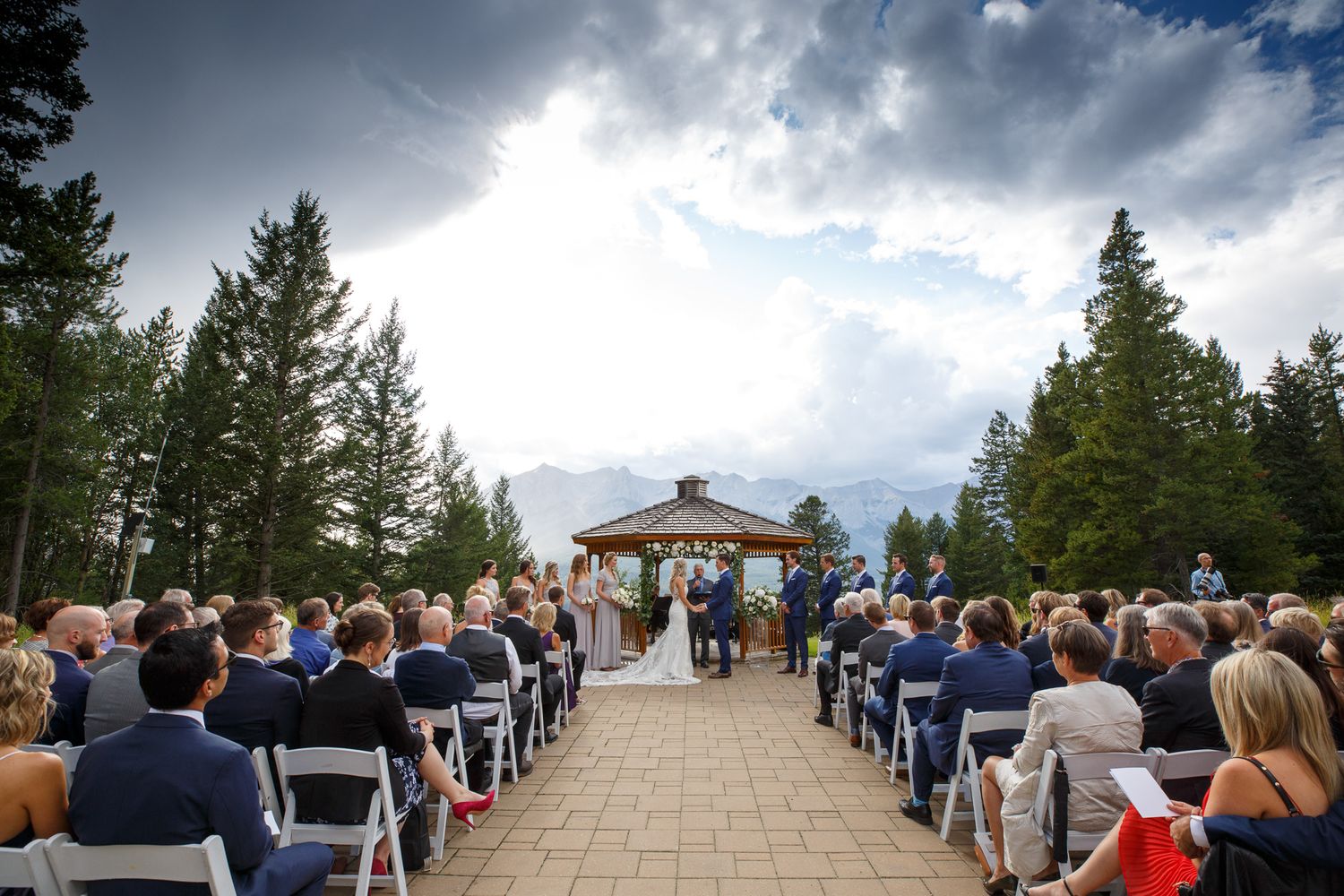 Outdoor wedding ceremony setup with rows of white chairs leading to a gazebo under dramatic cloudy mountain skies at Silvertip resort.