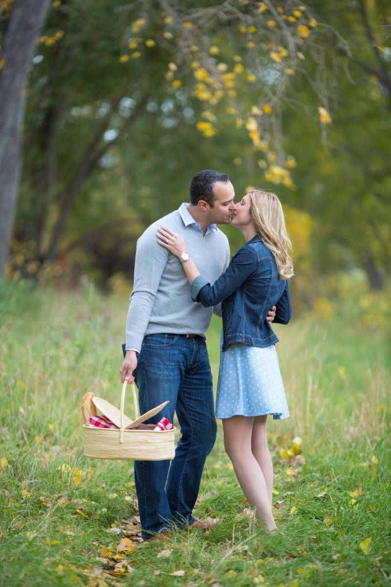 Couple sharing a romantic kiss in a park while holding a picnic basket during autumn at Fish Creek Park in Calgary.