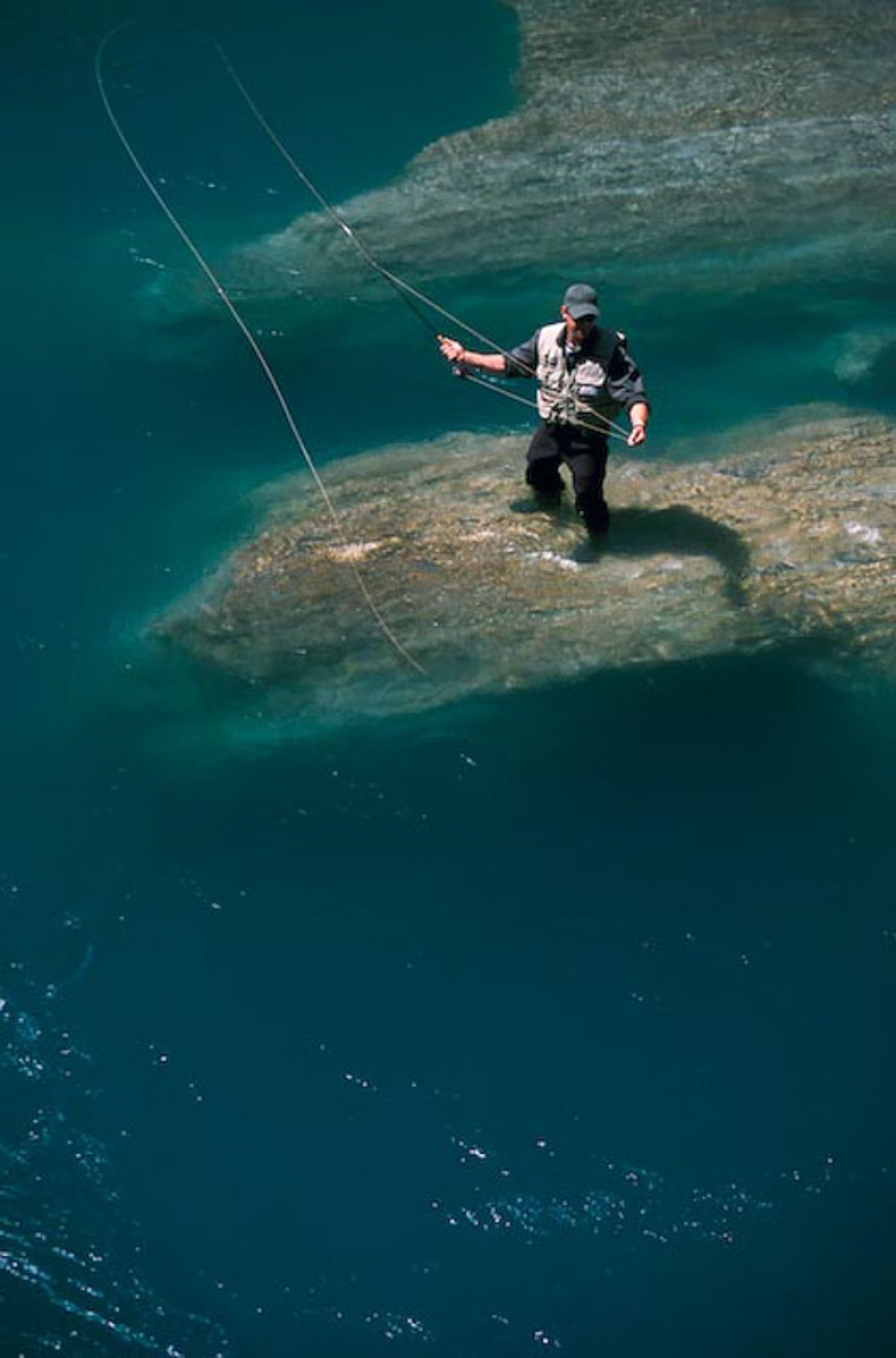 A fly fisherman throwing a line into turquoise ocean waters from a rocky ledge. Kootenay National Park, BC