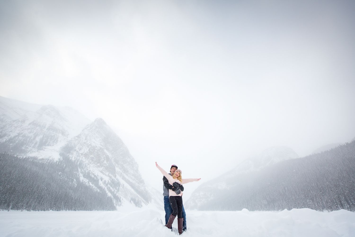 Snow-capped mountain peaks rise majestically through misty clouds in a dramatic winter landscape at Lake Louise.