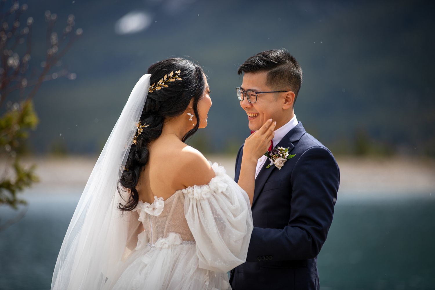 A romantic wedding moment captured outdoors by a serene lake in Canmore, AB with mountains in the background.
