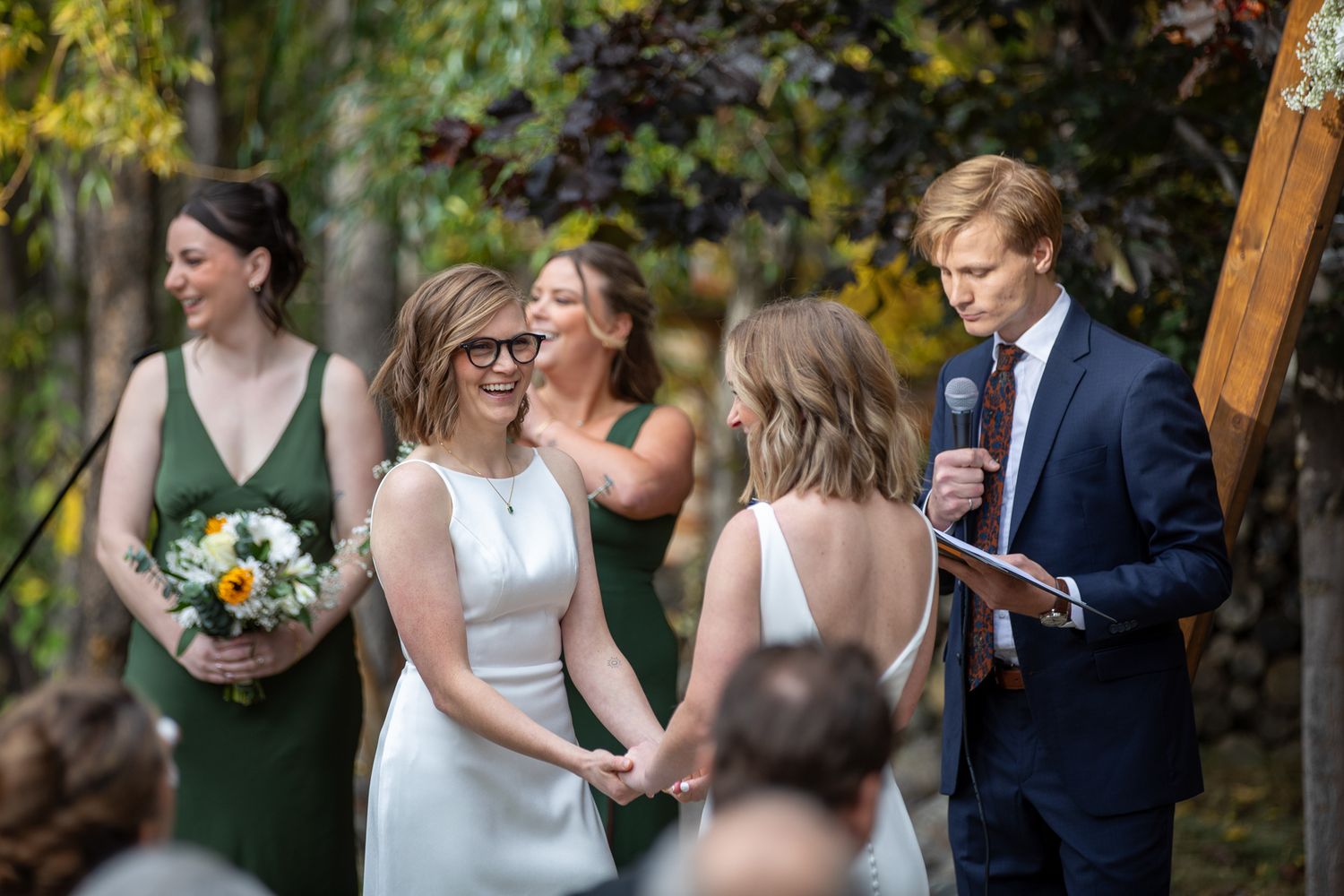 An outdoor wedding ceremony takes place in a garden setting with autumn foliage in the background. Earl Grey Lodge Panorama BC