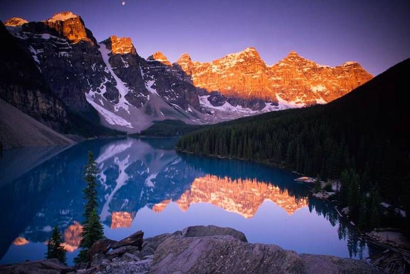 Stunning mountain peaks reflect in calm alpine lake waters during golden sunrise in Banff National Park. Moraine Lake.