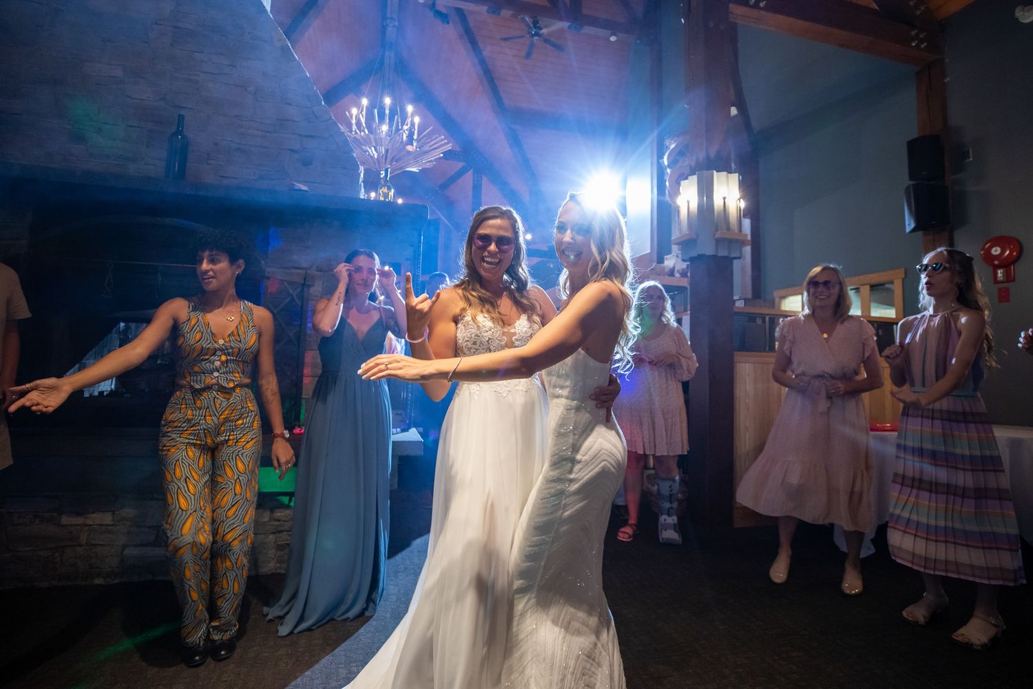 Bride in white wedding gown dancing joyfully with guests at elegant indoor wedding reception with blue lighting at Kicking Horse Resort, BC