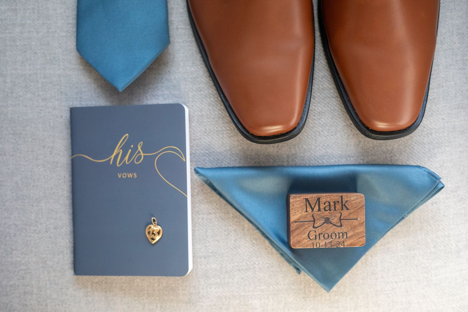 Wedding details including brown leather dress shoes, blue tie, vows book, and personalized pocket square on grey surface.  Canmore, Alberta.