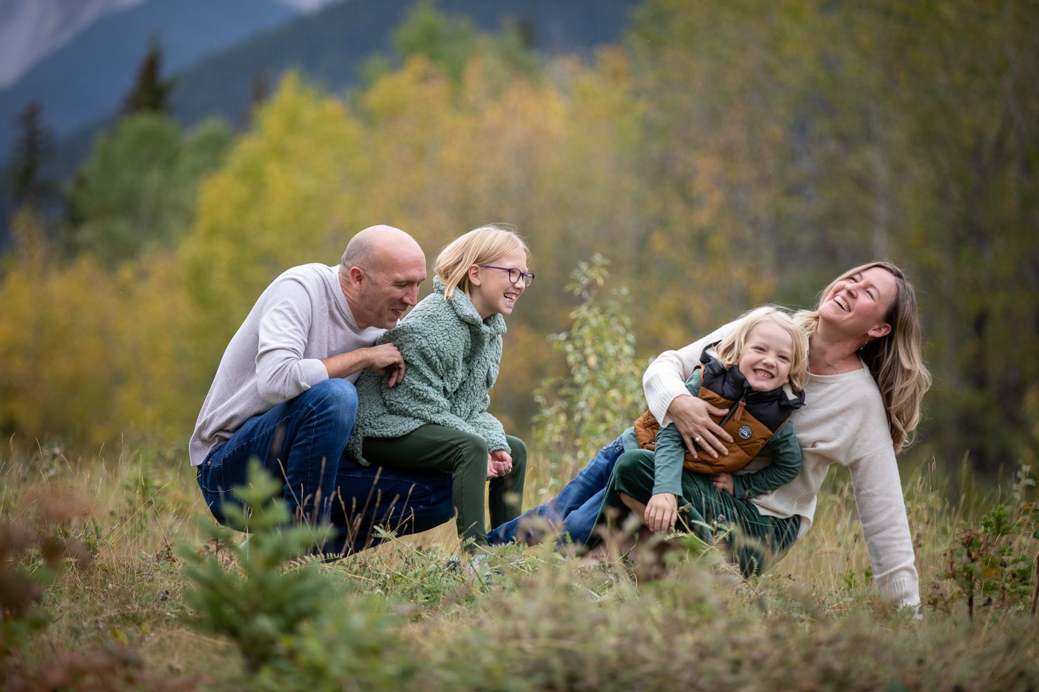 A couple lying in a field of wildflowers with mountains in the background during autumn at Quarry Lake Park, Canmore, AB.