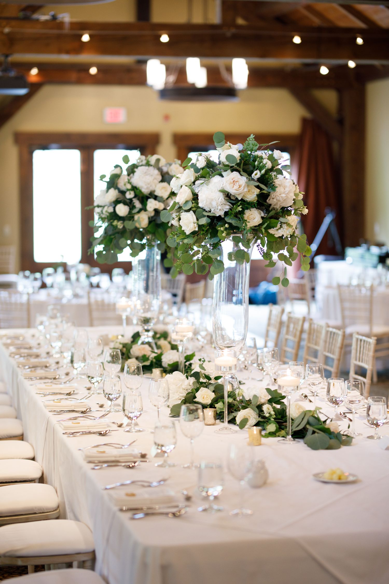 Elegant wedding reception tables decorated with white linens, floral centerpieces and chiavari chairs in a bright banquet hall. Silvertip.